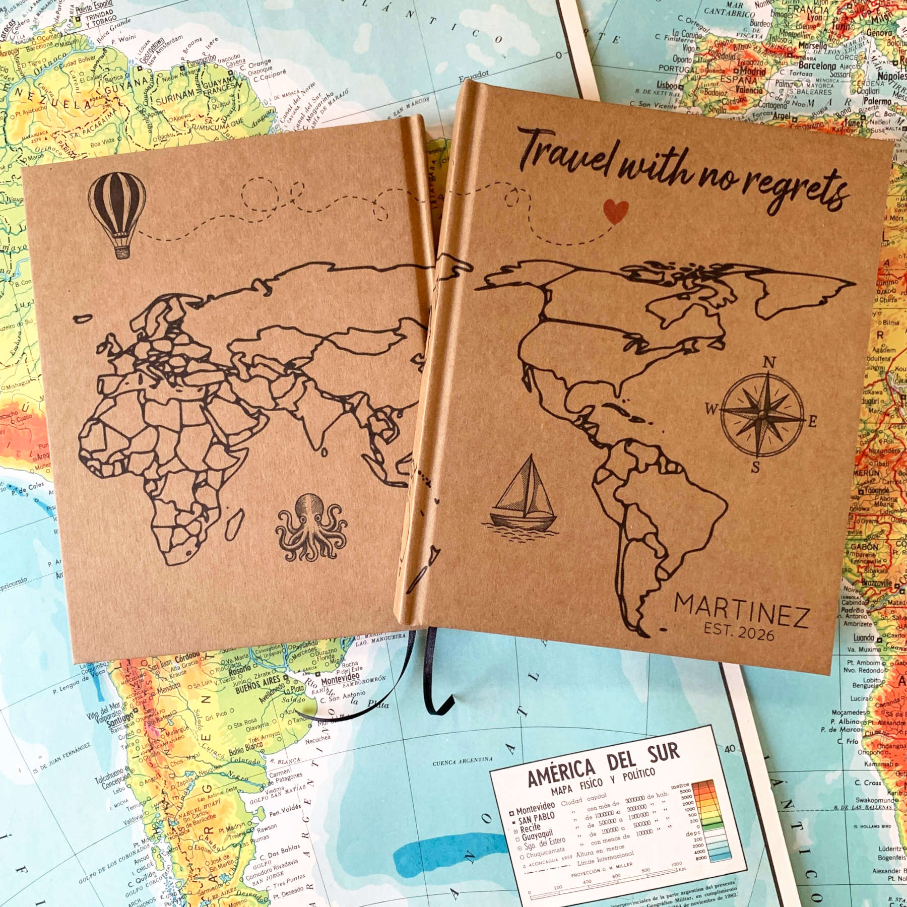 Two world travel journals, hardback, personalized, with world maps for coloring in. Custom cover text and artwork. Laying together on vintage world maps.